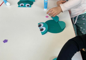 Dzieci przy stoliku wykonują pracę plastyczną - żaby