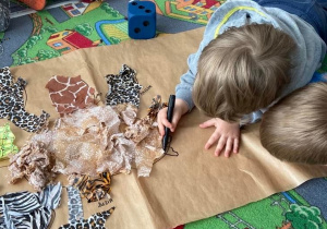 Chłopiec na dywanie rysuje po kartonie kontur Chochlika