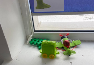 Zielone zabawki na parapecie umieszczone pod znaczkiem z zielonym ślimakiem