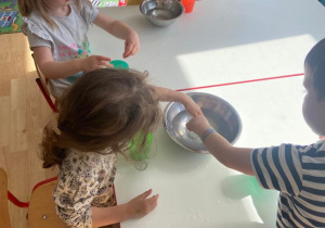 Dzieci przy stoliku wyławiają z metalowej miski żelowe kulki i umieszczają je w plastikowych kolorowych kubeczkach