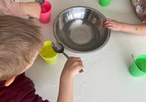 Dzieci przy stoliku wyławiają łyżkami żelowe kulki i umieszczają je w kolorowych plastikowych kubeczkach