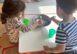 Dzieci wyławiają żelowe kuleczki z miski przy pomocy łyżek