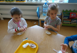 Sala przedszkolna. Dzieci siedzą przy stole i wysiewają owies wielkanocny.