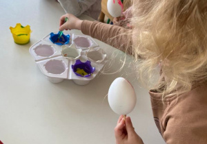 Dziewczynka z chłopcem przy stoliku maluje styropianowe jajka farbami