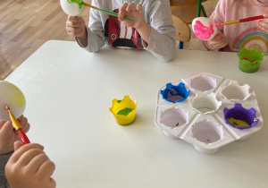 Dzieci przy stoliku malują styropianowe jajka farbami