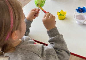 Dziewczynka z chłopcem przy stoliku maluje farbami styropianowe jajka