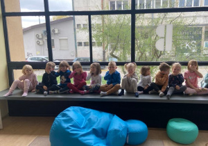 Dzieci siedzą w siadzie skrzyżnym i zakrywają usta