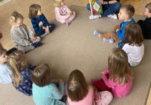 Dzieci w kole na dywanie słuchają czytanej przez Panią książki