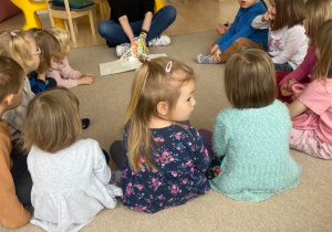 Dzieci na dywanie siedzą w kole i słuchają książki