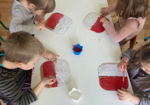 Dzieci przy stoliku malują kartoniki farbami w barwach narodowych - białym i czerwonym