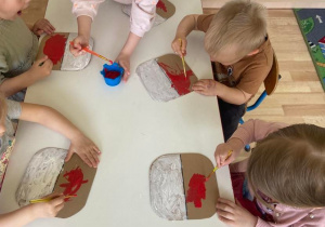 Dzieci przy stole malują na kartonie flagę Polski