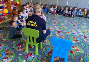 Strażnik Miejski siedzi na krzesełku przed dziećmi siedzącymi na dywanie