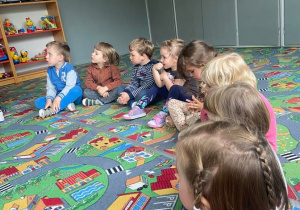 Dzieci w kole na dywanie słuchają książki