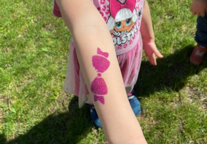 Dziewczynka w ogrodzie pokazuje brokatowy tatuaż na ręku - wzór kokardka
