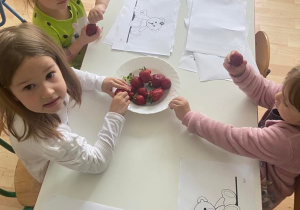 Dziewczynki przy stoliku jedzą truskawki i kolorują kolorowanki