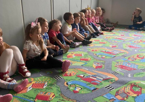 Dzieci siedzące na dywanie, słuchają czytanej książki