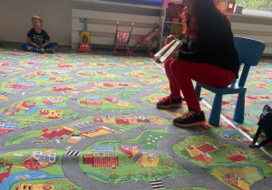 Mama dziewczynki siedząca na dywanie pokazuje dzieciom książkę