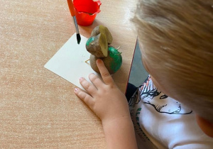 Chłopiec przy stole maluje figurkę żaby zrobioną z ziemniaka