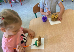Dziewczynki przy stole malują figurki z ziemniaka w kształcie żaby