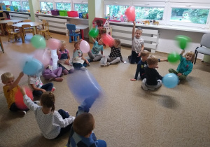 dzieci siedzą w kręgu, bawią się balonami