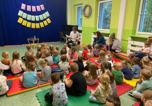 dzieci siedzą na materacach i słuchają książki czytanej przez Skrzata Makówkę