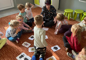 Dzieci na dywanie podają nauczycielce karty z obrazkami
