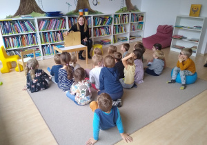 dzieci siedzą na dywanie i słuchają pani bibliotekarki