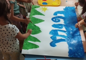 Sala przedszkolna. Dzieci malują farbami przy stole.