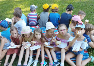 Dzieci siedzą na kocu w ogrodzie przedszkolnym i jedzą śniadanie.