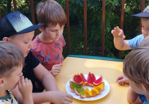 Dzieci siedzą przy stoliku na tarasie i jedzą "kolorowe galaretki"