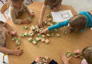 Dzieci układają literkę A z drewnianych klocków przy stolikach