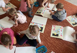 Dzieci na dywanie malują w książkach przygodę literki A