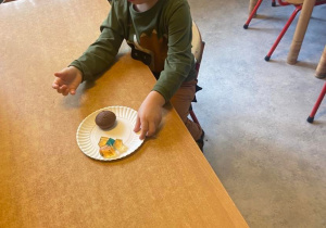 Chłopiec przy stoliku zjada czekoladową babeczkę