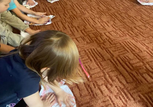Dzieci na dywanie rozprostowują papier ze zgniecionej kulki