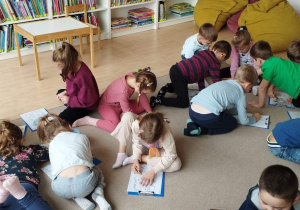 Sala w bibliotece Ferment. Dzieci siedzą na dywanie, kolorują kolorowankę o strusiu.