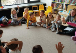 Sala w bibliotece Ferment. Dzieci siedzą na dywanie w kole, rozmawiają z panią prowadzącą spotkanie o treści zaprezentowanego opowiadania.