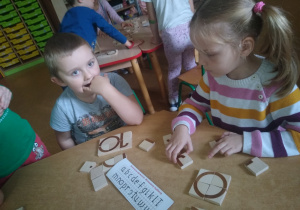dzieci przy stoliku układają litery z drewnianych klocków