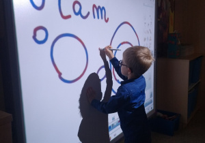 chłopiec przy tablicy interaktywnej pisze literę O