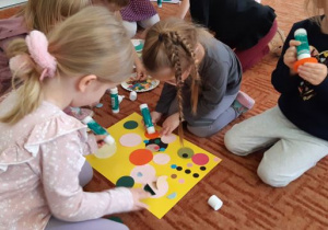 Dzieci przyklejają na karton kolorowe koła.