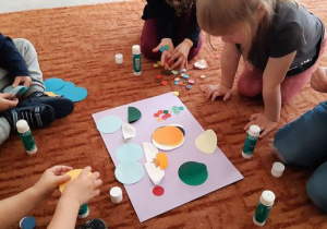 Dzieci przyklejają na karton kolorowe koła.
