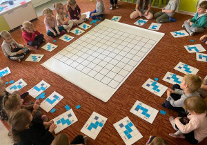 Dzieci siedzą na dywanie wokół maty do kodowania.