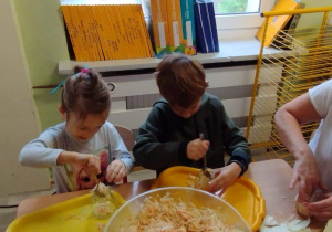 Sala przedszkolna. Dziewczynka i chłopiec siedzą przy stoliku i wkładają kapustę do słoików