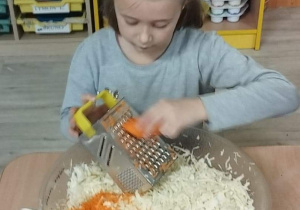 Sala przedszkolna. Dziewczynka siedzi przy stoliku i trze marchewkę