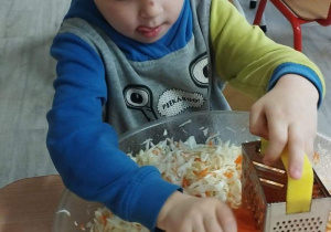 Sala przedszkolna. Chłopiec siedzi przy stoliku i trze marchewkę.