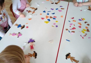 Dzieci ozdabiają piankowe postacie dzieci kolorowymi naklejkami ubranek