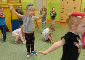 Dzieci poruszają się po sali gimnastycznej z woreczkami gimnastycznymi na głowach