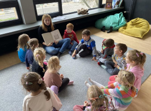 dzieci z edukatorką siedzą w kole na dywanie i oglądają książkę