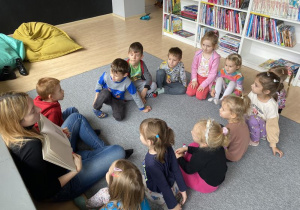 dzieci z edukatorką siedzą w kole na dywanie i oglądają książkę