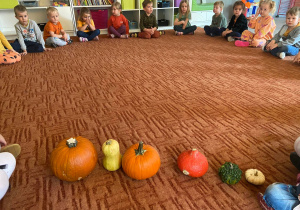 Dzieci w kole na dywanie przed nimi dynie o różnych kształtach i rozmiarach