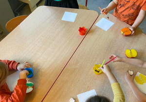 Dzieci przy stolikach malują połówki jabłek farbami